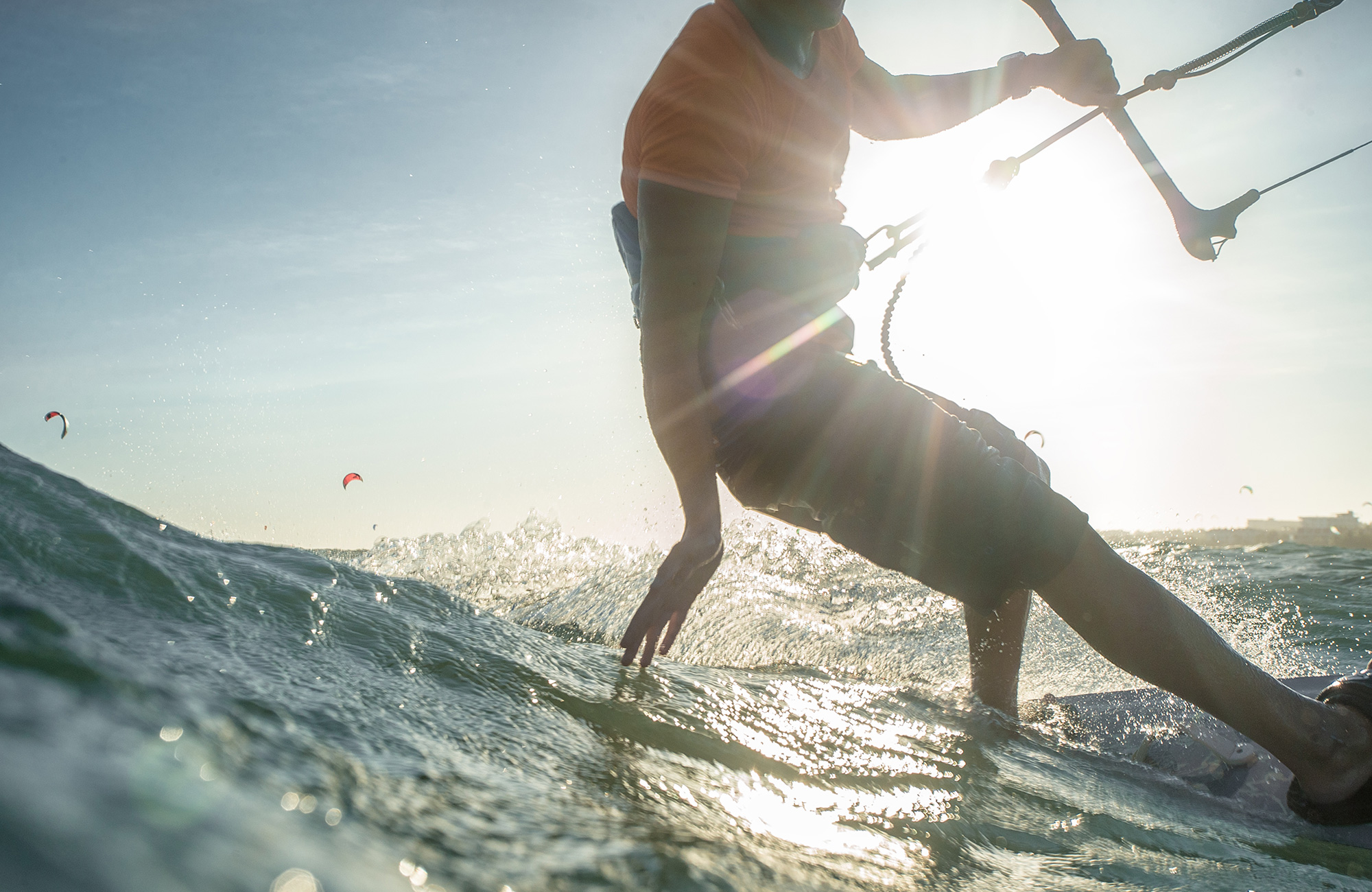 Maður sem er að kitesurfa erlendis snertir vatnið með fingrunum