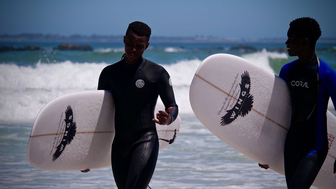 Tveir strákar að halda á surfbrettum í sjálfboðastarfi í Suður-Afríku