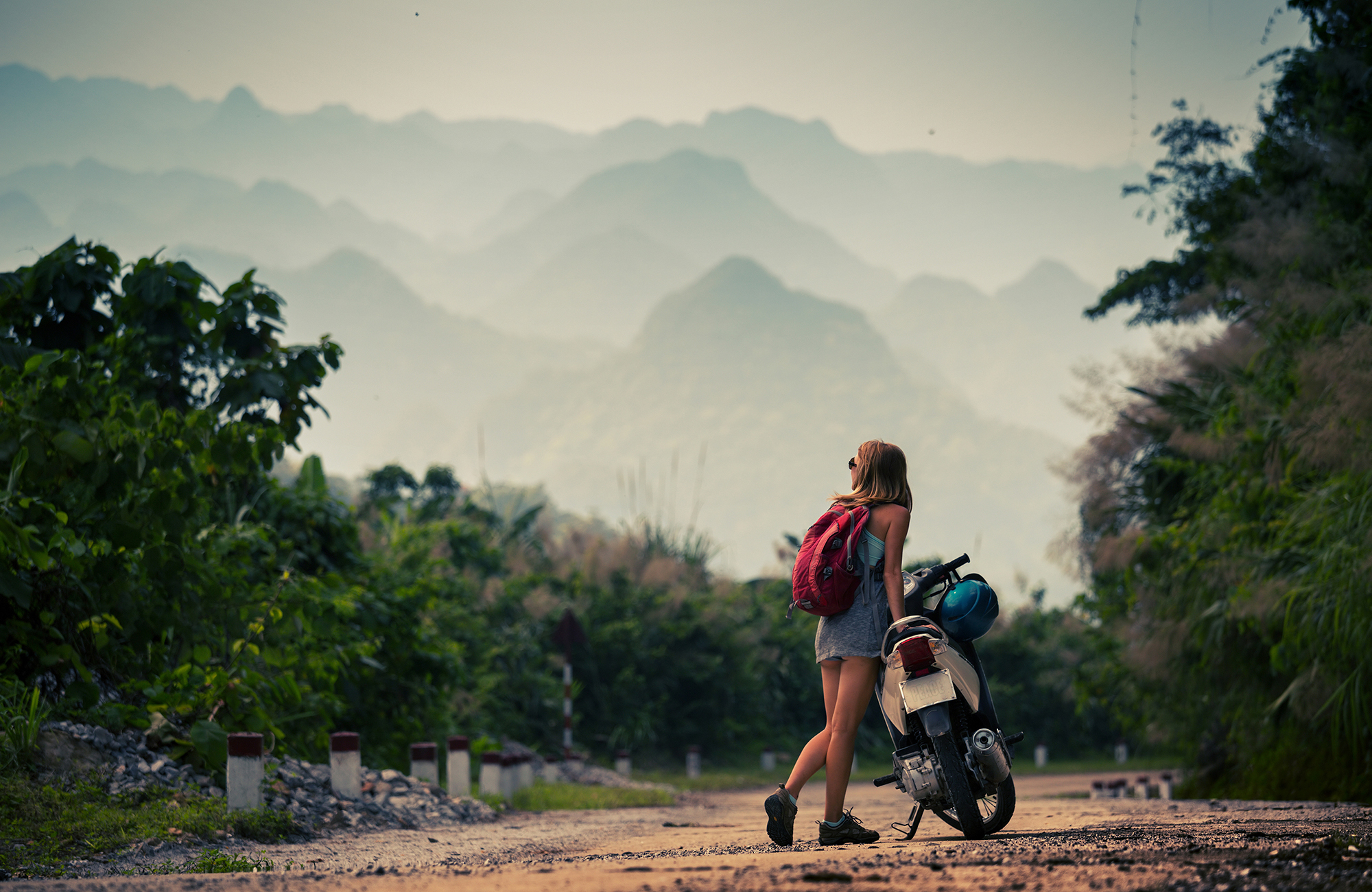 Girl with backpack on a scooter with mountains in the background