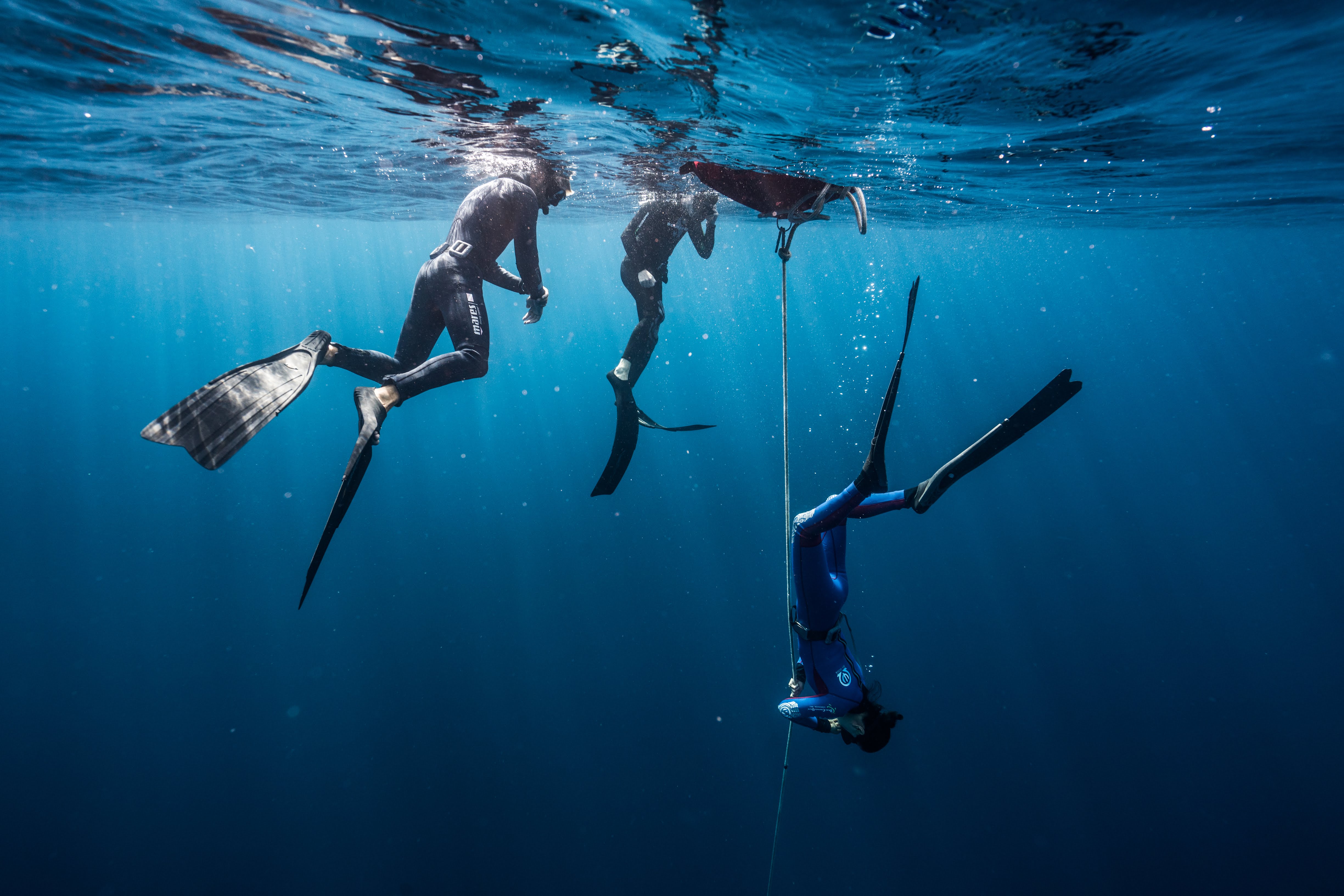 Three people freediving along a rope in a blue ocean in Indonesia